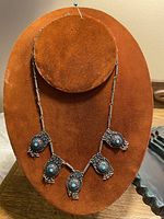 Front view of antique sterling silver necklace on display stand showing five turquoise set filigree pendants.