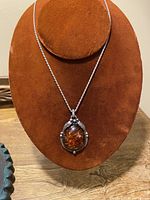 Front view of necklace displayed on a brown fabric bust showing amber pendant and silver chain.
