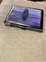 Angled view of the silver Ford cigarette box closed, showing the glossy purple top with Ford logo and attached lighter on the side.