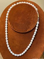 Full view of a 16 inch freshwater pearl necklace with white pearls on a brown circular display stand.