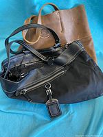 Photo showing the large brown leather Roots tote and the black nylon and leather handbag together on a blue background.