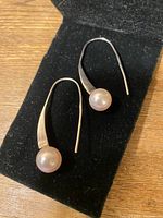 Pair of silver hanging earrings with rounded pearl on black felt surface.