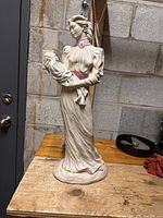 Full view of the ceramic mother and baby statue showing the standing mother figure holding the baby wrapped in cloth, dressed in white with pink accents.