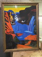 Framed original hand-painted abstract woman portrait by Emilien, showing a surreal fusion of landscape elements forming a woman's face with blue skin, red lips and intense eyes.