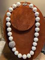 Full view of pearl necklace displayed on a stand showing white round pearls, rhinestone ball, and silver clasp.