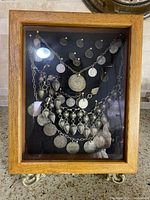 Frontal view of the shadowbox showing an assortment of antique Middle Eastern jewellery mounted on black fabric inside a wooden frame.