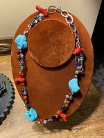 Necklace displayed on a brown velvet stand showing large turquoise, coral, and assorted gem stone beads on silver links.