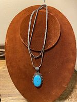 Full view of silver chain necklace with turquoise pendant on display stand.