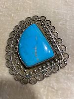 Close-up of the turquoise stone brooch/pendant showing the blue triangular stone and intricate silver filigree border.