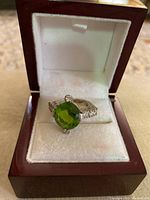 Front view of vintage 925 silver ring with large faceted green stone and small clear zirconia stones, displayed in a dark wooden box with white velvet interior.