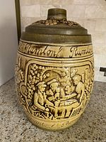 Front view of ceramic cookie jar with embossed relief of people, grapevines, and Rumton script