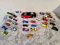 Overview of all 31 diecast cars spread on grey surface including large Bugatti and one packaged Hot Wheels car