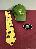 Photo of the three items: John Deere green hat, yellow tie with tractor motifs, and the belt buckle.
