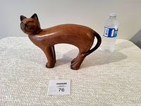 Side view of the large vintage wooden cat carving placed next to a water bottle for size comparison on a white textured surface.