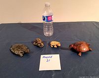Four turtle sculptures on table with water bottle for scale