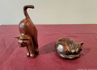 Photo of two wooden cat carvings on a maroon surface, showing the scared cat and sleeping cat figurines.