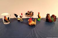 Full lot displayed on dark cloth showing all six items including porcelain mug, several figurines, key rack, and wooden carving.