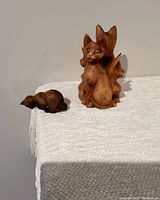 Photo of both wooden cat carvings placed on a white cloth surface showing size and details.