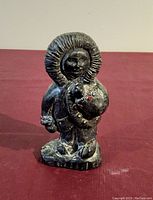 Front view of the dark soapstone Inuit carving showing detailed parka hood, face, and figure holding an object with painted bead details