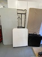 Three folding tables and two cushions arranged standing upright, showing various sizes and cushions in beige and black