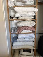 Shelf filled with assorted pillows in white and beige tones stacked, some pillowcases folded beside.