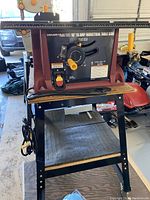 Front view of the Chicago Electric 10 inch 15 amp industrial table saw mounted on Central Machinery rolling tool stand showing control panel, power cord, and wooden shelf below.