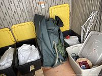 Four plastic storage bins with yellow and gray lids filled with wrapped Christmas tree parts and cords.