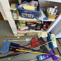 Full view of cleaning supplies including mops, brooms, dustpans, towels spread on floor and shelves.
