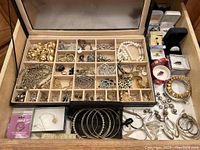 Open wooden jewelry case showing compartments filled with rings, earrings, bracelets and necklaces