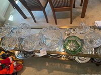 Overhead view of various crystal and cut glass bowls and dishes arranged on glass table with metal frame.