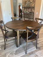 Photo showing the round wooden dining table with four matching wooden chairs with metal cross-back supports, arranged around the table.