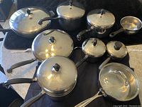 Full set of Farberware stainless steel pots and pans with lids and black handles. Includes Palm Restaurant sauce pan with stainless steel handle on right side.