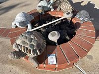 Top down photo showing all five turtle sculptures arranged on and around a circular brick and stone fire pit or planter area with solar garden lights.