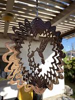 Close-up photo of a metal hanging decoration with a cut-out hummingbird and flowers design, showing its rusted, weathered patina.