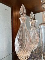 Clear view of two round crystal decanters with pointed teardrop stoppers and detailed cut glass patterns