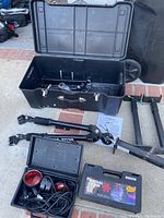 Photo showing black plastic case, tow bar parts with joints and arms, instruction manual, separate black plastic case with red emergency flashers, and rectangular black plastic case labeled Radial Chain tire chains.