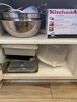 Photo showing nested stainless steel mixing bowls with a KitchenAid hand mixer in box, and another mixer with beaters attached on top of bowls.