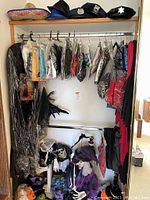 Full view of hanging costumes on rack including numerous wrapped costumes and multiple hats on top shelf including sombrero, police hats, and blue hats. Skeleton and witch decor at bottom of closet.