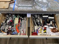 Two open wooden drawers filled with kitchen utensils including scissors, thermometers, clips, tongs, and other cooking tools.