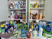 Wide view of cabinet shelves and counter space packed with assorted cleaning products including bottles, sprays, sponges, and boxes.