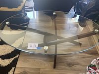 Front angle showing entire glass top and wood base on floor with partial rugs and furniture in background.