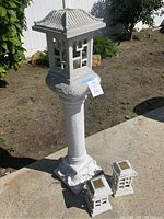 Large pagoda style stone and plaster garden solar light with two smaller matching units on ground beside it, showing overall detail and condition.