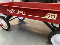 Close up photo of red Radio Flyer 90 wagon showing logo and wheels on concrete floor.