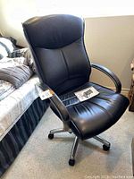 Front angled view of the black leather executive office chair showing seat, backrest, armrests, caster wheels and overall condition.