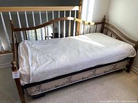 Front view of the oak wood twin trundle bed with white sheet covering the mattress and part of the bed frame visible.
