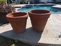 Two large terracotta clay pots side by side outdoors by pool, one empty and one with soil