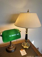Photo showing both lamps on a wooden table, green bankers lamp to the left, brass Stiffel lamp with beige shade to the right.