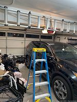 Cosco extending ladder folded and hanging over garage door, showing folded condition and black plastic end caps.