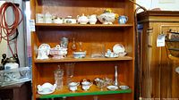 Full shelf with various china, crystal, and glassware including spice jars, tureen, candle holders, and vases