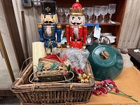 Full display of basket with assorted Christmas decorations including two nutcrackers, candle, ornaments, and wreath stand
